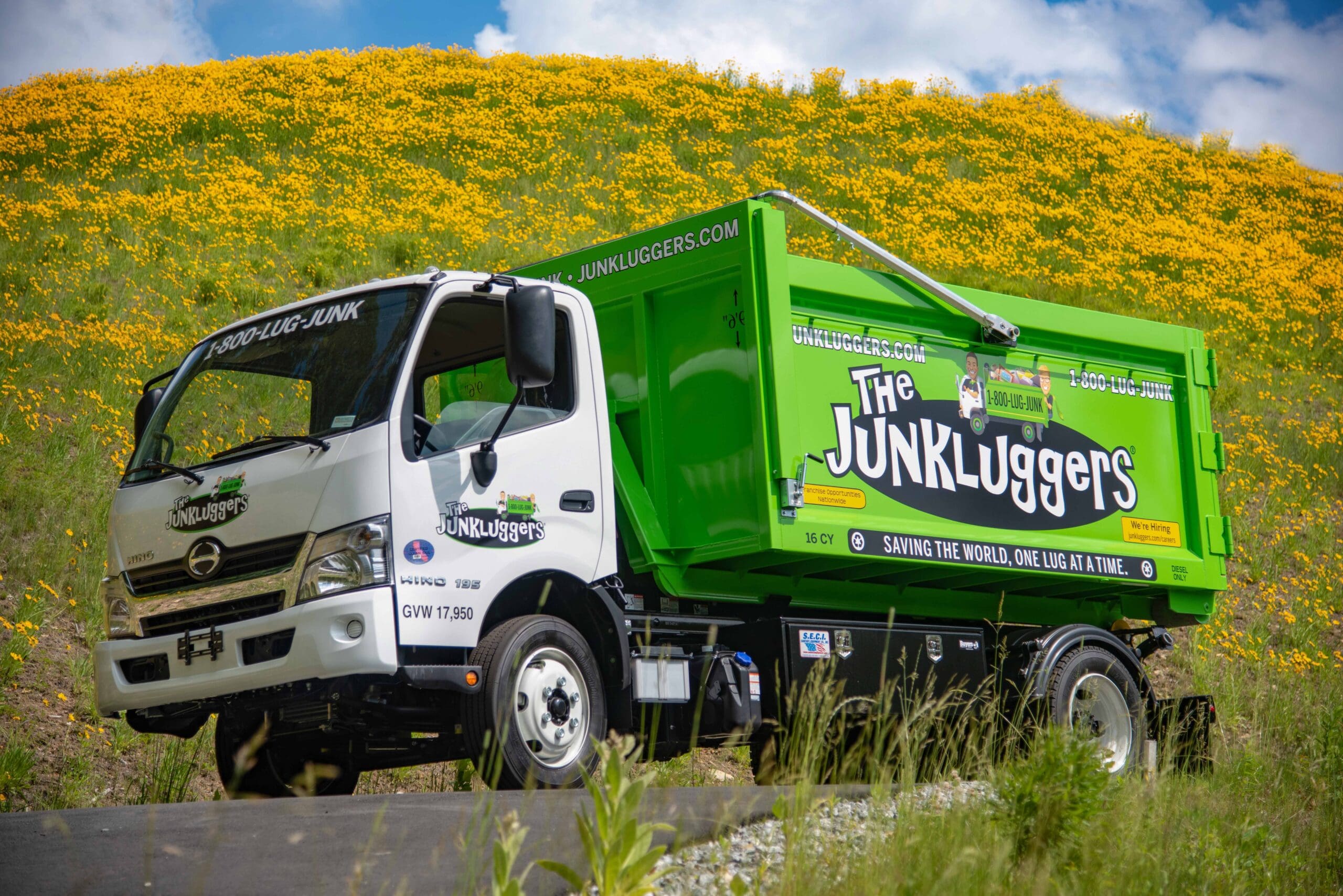 A large green truck in front of a field of yellow flowers